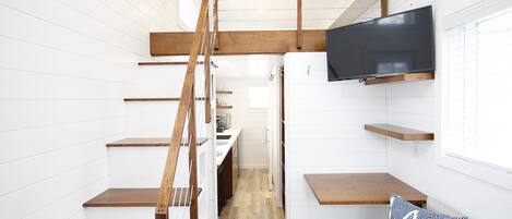 A compact, modern interior with a wooden staircase, built-in shelves, a flat-screen TV, and a cozy seating area.