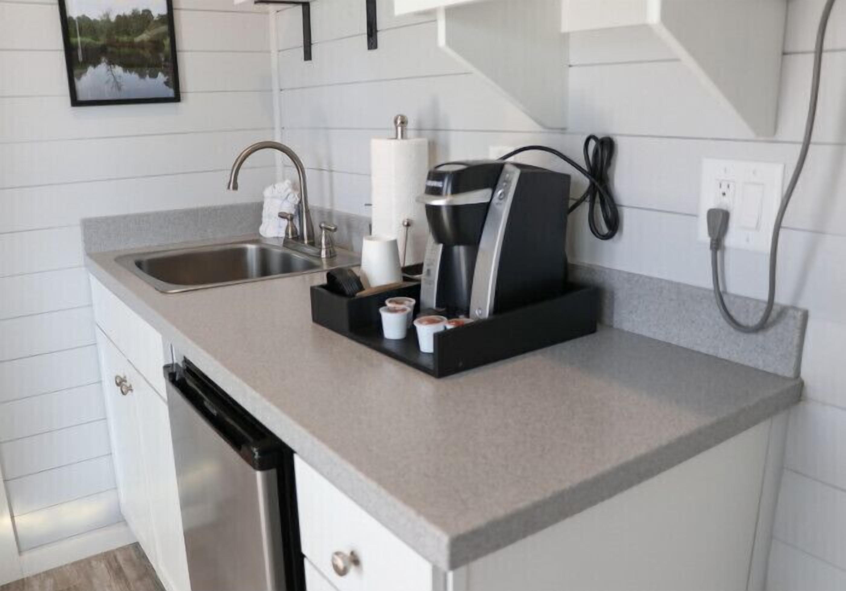 Una cocina con un lavaplatos de acero inoxidable, una cafetera y un escurreplatos.