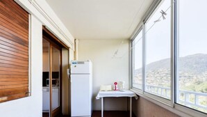 Un pequeño balcón con refrigerador, una mesa con cafetera y vistas a un paisaje montañoso.