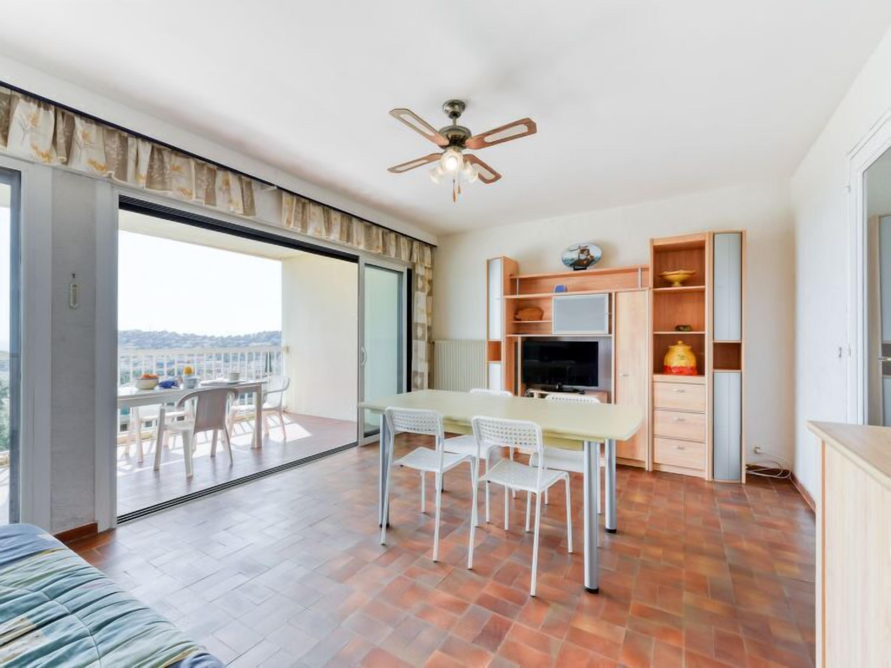 A modern apartment with a balcony, a dining area, a TV, and a ceiling fan.