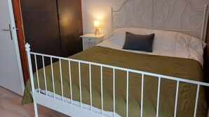 A bedroom with a white metal bed frame, a green bedspread, a white pillow, and two wall-mounted lamps. - Le Sporting by Interhome (Saint Gervais)