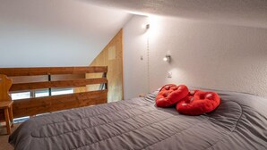 A bedroom with a sloped ceiling, a wooden headboard, a gray bedspread, and two red pillows. - Asters 1203 Bâtiment B4 by Interhome (Les Menuires)