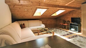 A cozy loft-style room with a sofa, a coffee table, and a TV. There are skylights on the ceiling, and a small dining area with chairs. - Obernberg by Interhome (Obernberg am Brenner)