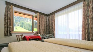 A hotel room with two beds, a table with a red tablecloth, a chair, and a window with a view of a forest. - Obernberg by Interhome (Obernberg am Brenner)