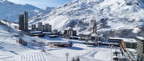 A snow-covered ski resort with modern buildings, ski lifts, and a mountain backdrop.