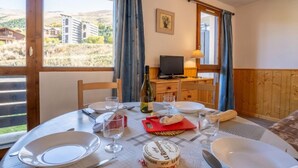 A dining area with a table set for two, a television, and a view of buildings through the window. - Sarvan 315 by Interhome (Les Menuires)