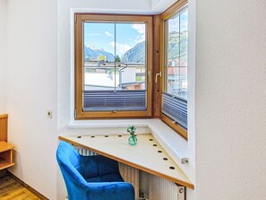 Une pièce d’angle avec une fenêtre, une chaise bleue et une petite plante.