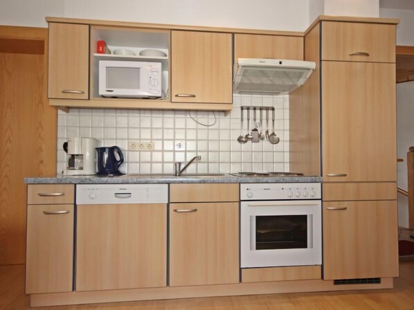 A compact kitchen with wooden cabinets, a microwave, a stove, and a coffee maker. - Apartment Handle by Interhome (Ried im Oberinntal)