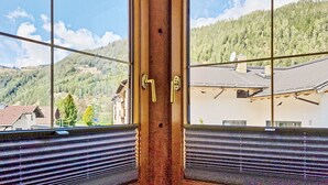 Une fenêtre donnant sur un paysage montagneux, une porte en bois avec une poignée en laiton et un store.