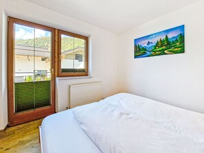Une chambre à coucher avec un lit, une fenêtre avec des stores, un radiateur et un tableau accroché au mur.