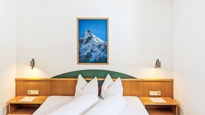 Une chambre d’hôtel comprenant un lit, deux tables de chevet, une tête de lit, un tableau représentant une montagne et des lampes fixées au mur.