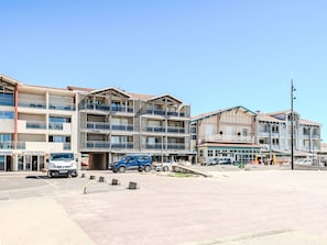 A multi-story building with balconies, a parking area, and various storefronts. - Horizon by Interhome (Mimizan)