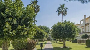 A pathway leading through a well-maintained garden with various trees and a building in the background. - Brisamar - Novo Sancti Petri by Interhome (Chiclana de la frontera)