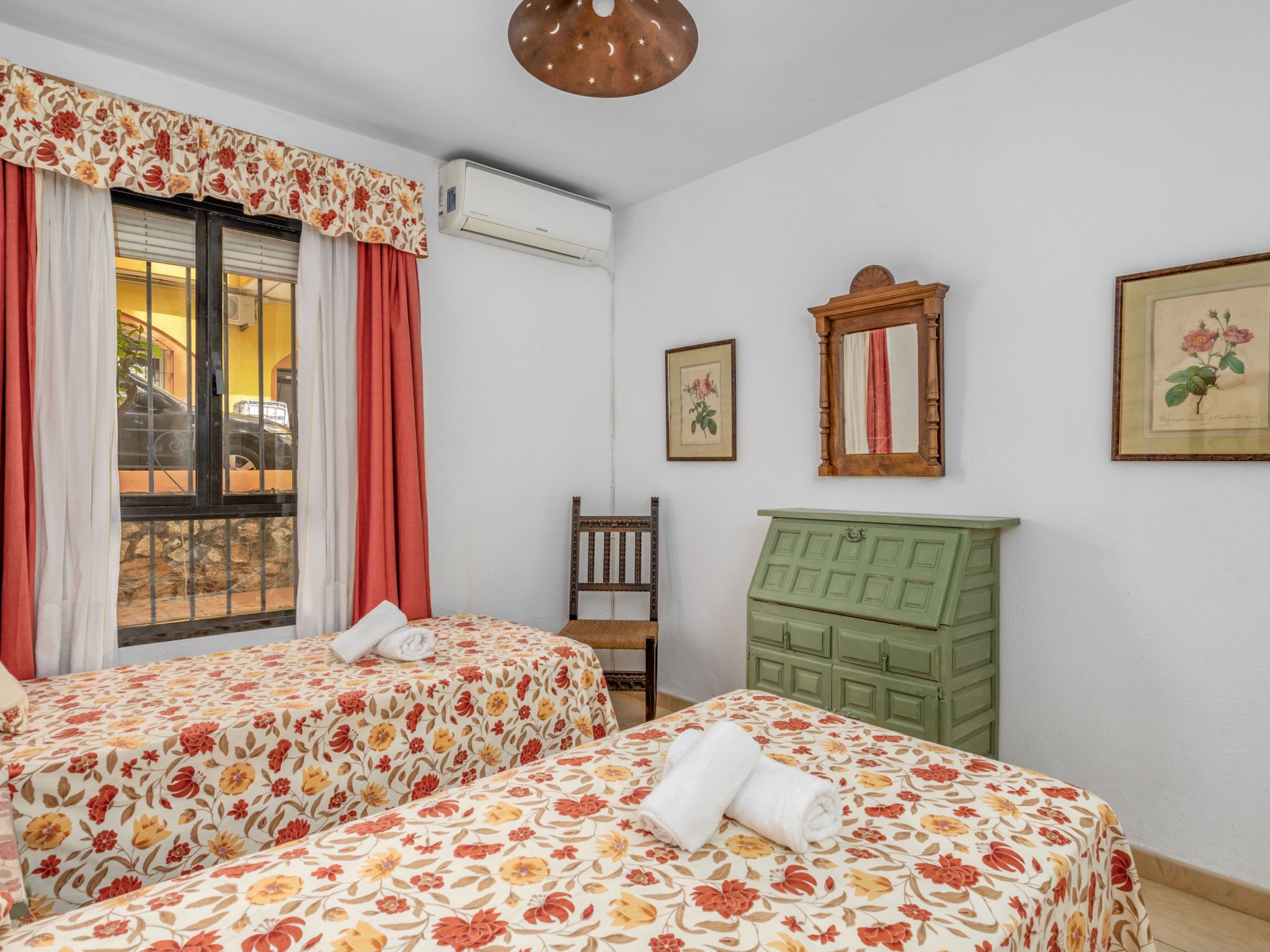 Una habitación con dos camas, un aparador verde, una silla de madera y un aire acondicionado de pared.