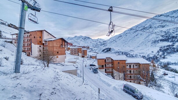En snedækket bjergby med moderne bygninger, en skilift og en vej med biler.