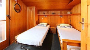 Une chambre de style cabane en bois, avec deux lits, un miroir rond et une petite étagère sur laquelle sont posés quelques objets.