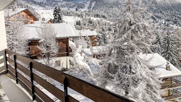 Un village de montagne enneigé, avec des chalets en bois et un balcon offrant une vue panoramique sur les environs.