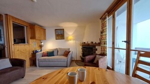 Un salon chaleureux avec une table en bois, deux canapés, une cheminée et de grandes fenêtres.