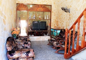 A living room with a stone wall, a television, and wooden furniture. - Casa Chicho Pega Duro (Trinidad)