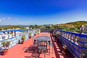 A rooftop terrace with a table and chairs, potted plants, and a view of distant hills and buildings. - Casa Chicho Pega Duro (Trinidad)