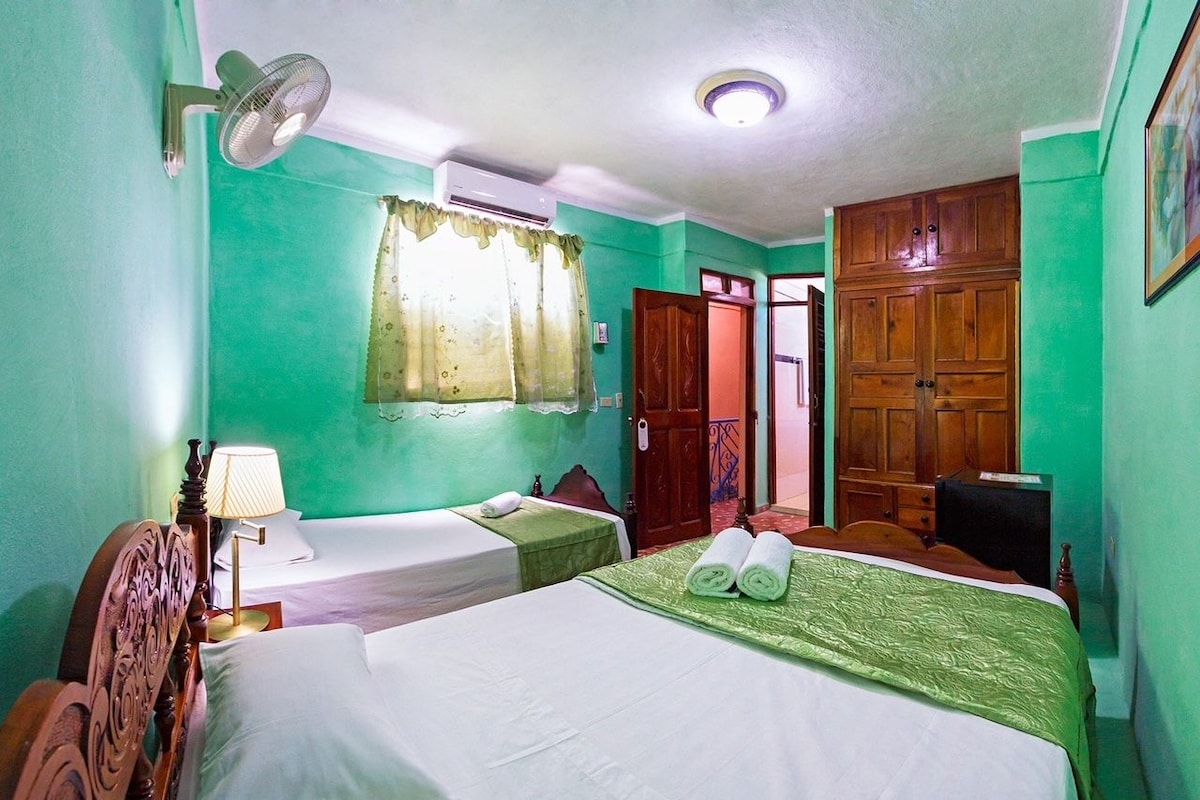 A hotel room with two beds, a wooden wardrobe, a ceiling fan, and a window with curtains.