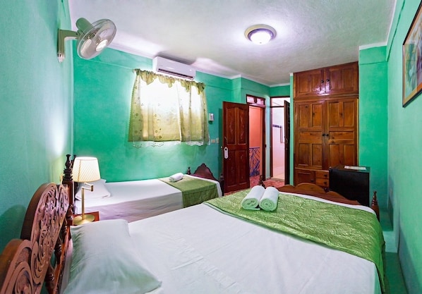 A hotel room with two beds, a wooden wardrobe, a ceiling fan, and a window with curtains. - Casa Chicho Pega Duro (Trinidad)