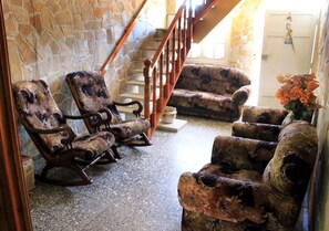 A stone-walled interior with a wooden staircase, rustic wooden chairs, and a vase with flowers. - Casa Chicho Pega Duro (Trinidad)