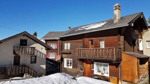 A wooden chalet with a balcony, a chimney, and a snow-covered ground.