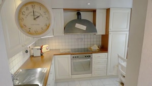 A kitchen with white cabinets, a stainless steel sink, a built-in oven, and a clock on the wall.