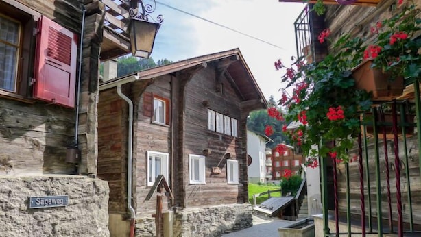 A traditional wooden building with a stone foundation, a sign reading "Sägeweg," and a small garden with red flowers.