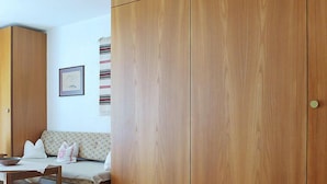 A room with a wooden wardrobe, a sofa, a table, and a wall-mounted picture. - Castor und Pollux by Interhome (Täsch)