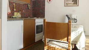 A compact kitchen with wooden cabinets, a built-in oven, and a small dining area with a table and chair. - Castor und Pollux by Interhome (Täsch)