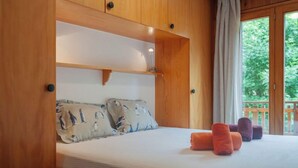 Un dormitorio con cabecera de madera, una cama con ropa de cama blanca, dos almohadas con estampado de pingüino y vistas a zonas verdes al exterior.