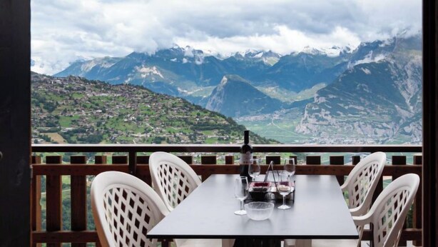 Una mesa con cuatro sillas y una botella, con una montaña como fondo.