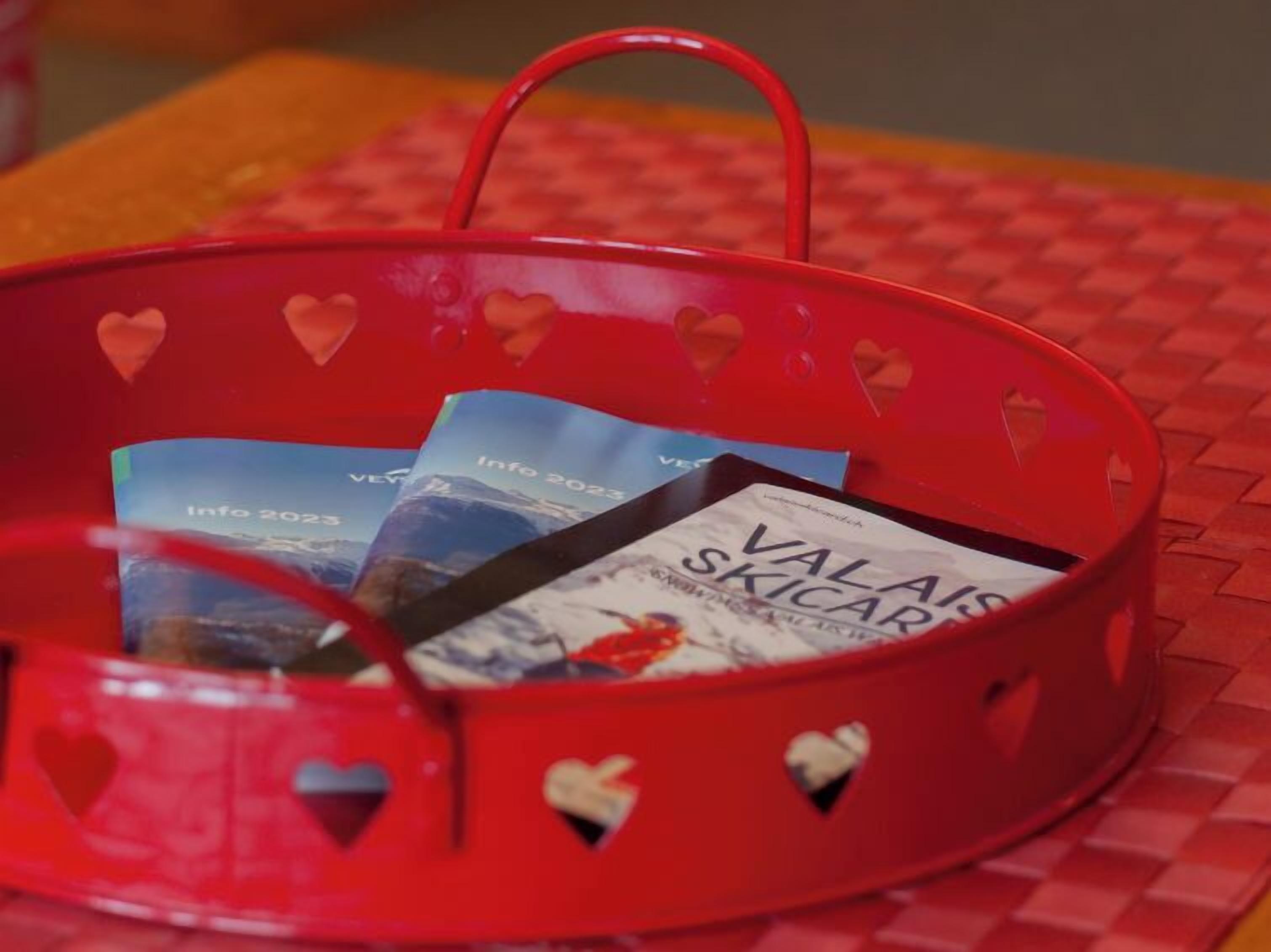 A red basket with heart-shaped cutouts containing brochures.