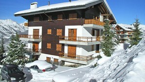 Una chaleta de varios pisos con techo inclinado, balcones de madera y un paisaje cubierto de nieve.