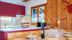Una cocina moderna con armarios rojos, una mesa de comedor de madera dispuesta para cuatro personas, y un ventanal con vistas a edificios.