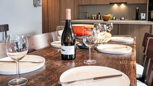 Une table à manger dressée avec des verres à vin, des assiettes et des couverts, et une bouteille de vin placée au centre.