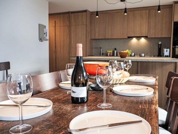 Una mesa de comedor dispuesta con copas de vino, platos y cubiertos, con una botella de vino en el centro.