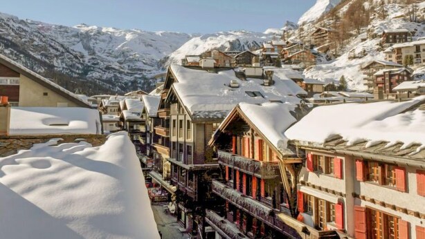 Un village de montagne enneigé, avec des bâtiments traditionnels en bois et un sommet imposant en arrière-plan.