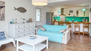 Un salon moderne avec un canapé, une table basse et un coin repas, la cuisine étant visible au fond.