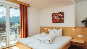 Quarto de hotel moderno com uma cama grande, um quadro na parede e vista para montanhas pela janela.