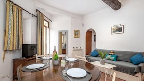 A dining area with a round table set for two, a sofa, and a television in a living room. - Rue de la Pompe by Interhome (Antibes)