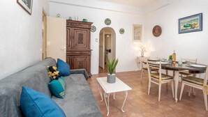 A cozy living room with a grey sofa, a dining table with chairs, and a kitchen area with wooden cabinets. - Rue de la Pompe by Interhome (Antibes)