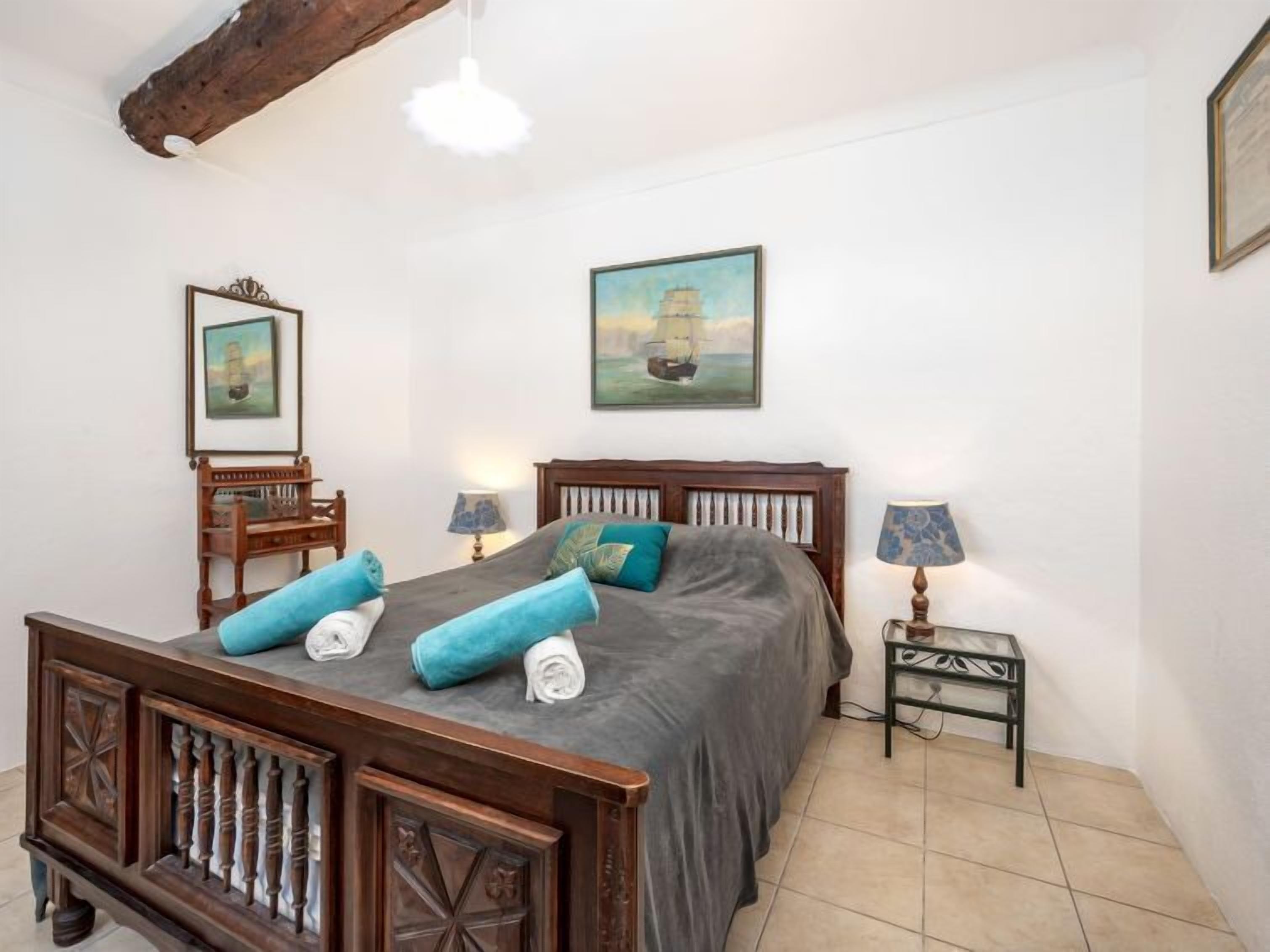 A bedroom with a wooden bed, two bedside tables with lamps, a painting on the wall, and a mirror above the bed.