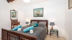 A bedroom with a wooden bed, two bedside tables with lamps, a painting on the wall, and a mirror above the bed. - Rue de la Pompe by Interhome (Antibes)