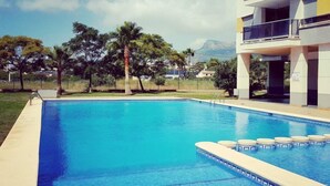 A swimming pool with clear blue water, surrounded by a low fence, and a multi-story building with balconies in the background. - Costa Calpe by Interhome (Calpe/Calp)