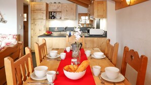 A wooden dining table with a red runner, surrounded by wooden chairs. There are white bowls, cups, and a basket of bread on the table. - Boule de Neige by Interhome (Verbier)