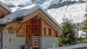 A wooden chalet with a snow-covered roof, a wooden staircase, and a view of snow-covered mountains. - Boule de Neige by Interhome (Verbier)