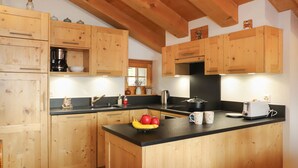 A kitchen with wooden cabinets, a central island with fruit and mugs, a coffee maker, and a toaster. - Boule de Neige by Interhome (Verbier)